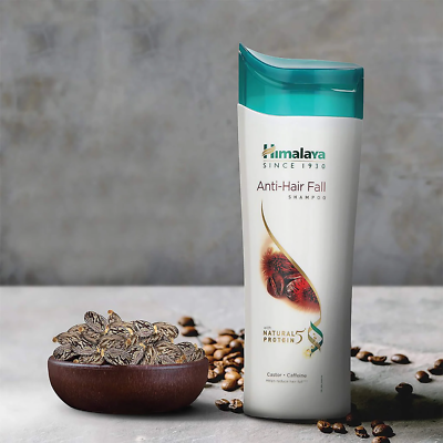 Himalaya Anti-Hair Fall shampoo bottle with a bowl of seeds and coffee beans on a gray background