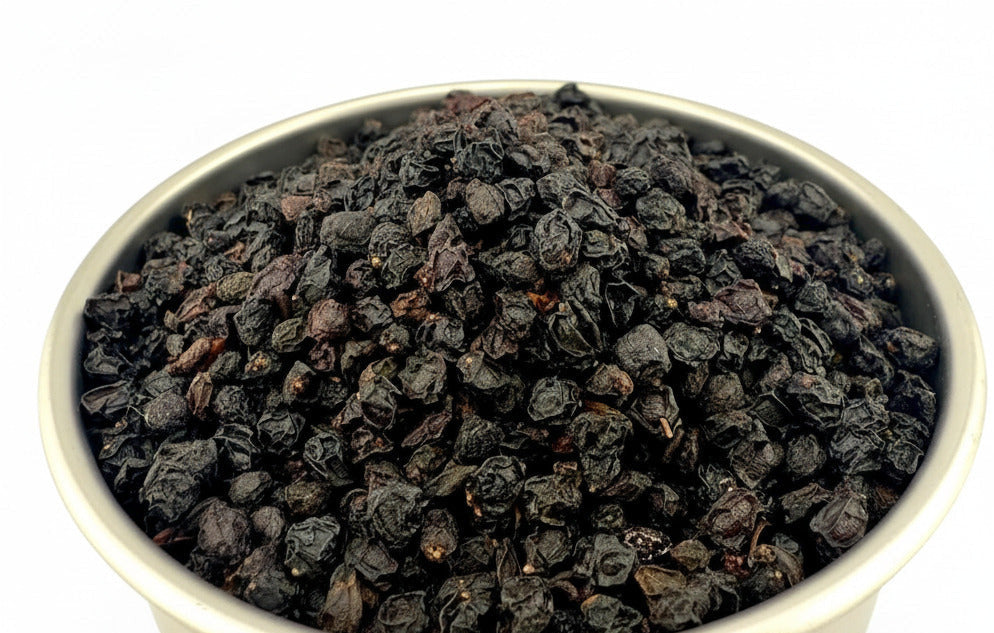 A metal bowl filled with dark, shriveled dried tea leaves, photographed on a plain white background. A faint 'wholesales' watermark is visible across the lower center.
