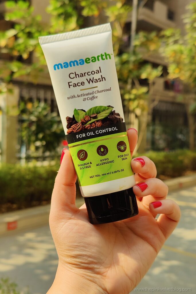Hand holding a tube of Mamaearth Charcoal Face Wash with blurred outdoor background