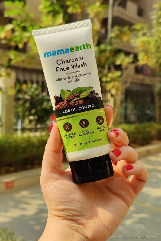 Hand holding a tube of Mamaearth Charcoal Face Wash with blurred outdoor background