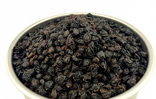 A metal bowl filled with dark, shriveled dried tea leaves, photographed on a plain white background. A faint 'wholesales' watermark is visible across the lower center.