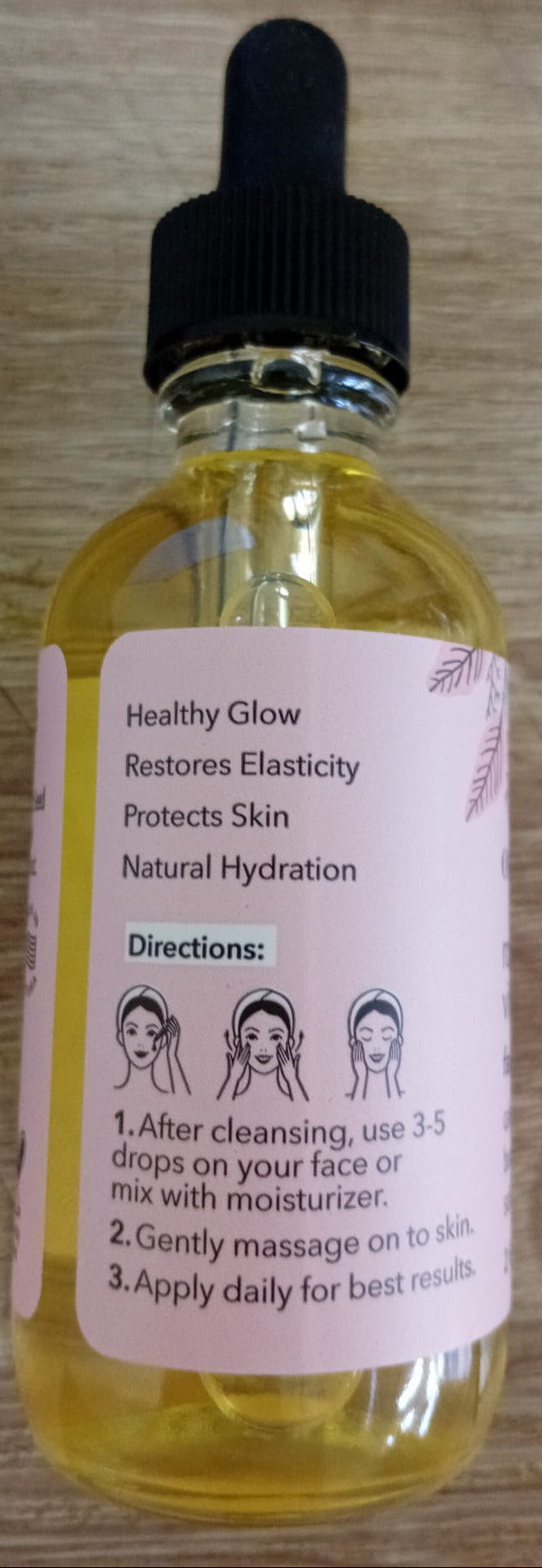 A small dropper bottle of Healthy Glow facial serum with a black cap and a pink label, placed on a wooden surface.