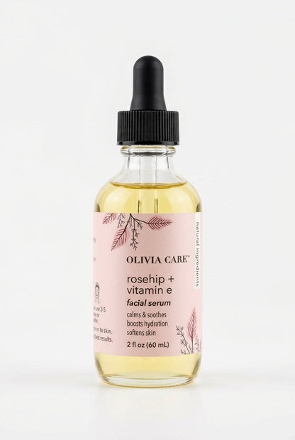 Olivia Care Rosehip + Vitamin E Facial Serum in a clear glass dropper bottle with a black cap and a light pink label, resting on a light wood surface.